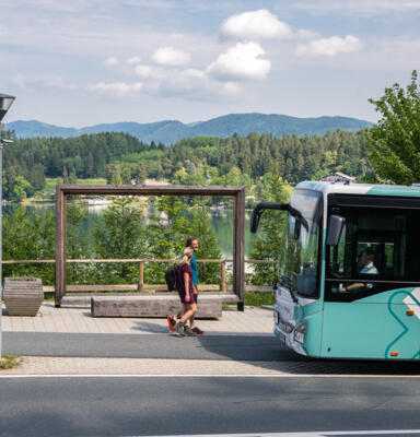 14_©Stabentheiner Zwei Personen vor einem Regionalbus an einer Haltestelle vor Seen- und Berglandschaft