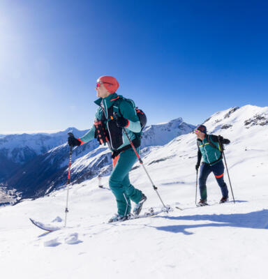 26_NPHT_Martin Lugger Zwei Personen mit Skiern steigen auf einem verschneiten Berghang auf.