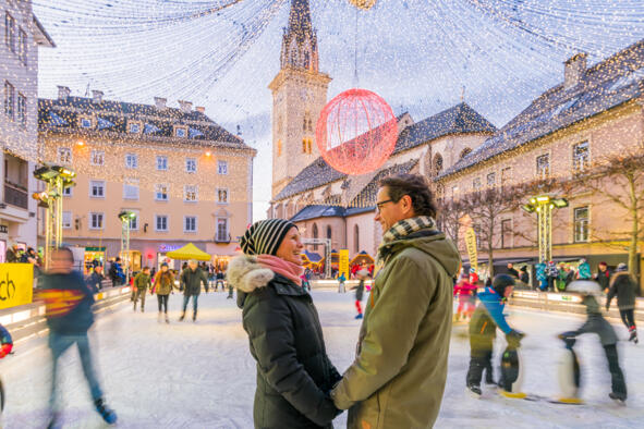 12_Kärnten Werbung GmbH_Michael Stabentheiner Zwei Personen auf einem festlich beleuchteten Platz mit Eislaufbahn in einer Kärntner Altstadt